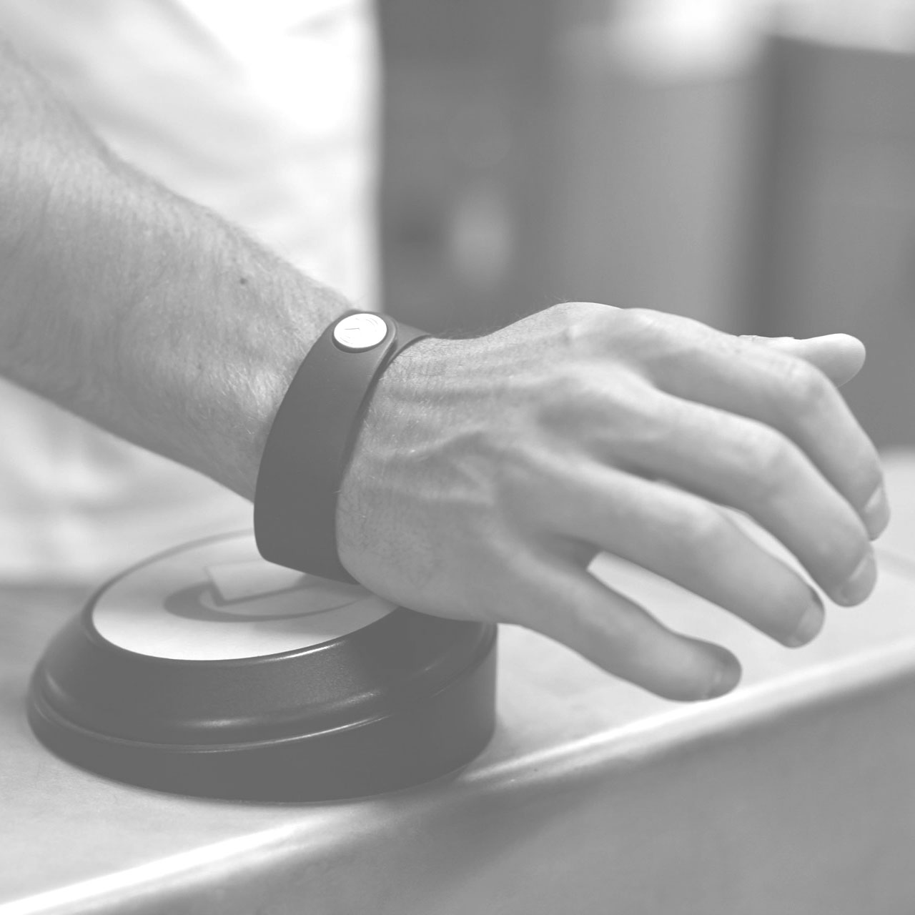 A black & white photograph of a man using a Barclays bPay Band at Transport For London - TFL. Source: Gizmodo, 2014. - https://www.gizmodo.co.uk/2014/09/public-service-announcement-london-tubes-trains-and-dlr-go-contactless-tomorrow/